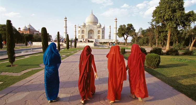 Cuatro mujeres en saris coloridos caminando hacia el Taj Mahal por un sendero de piedra