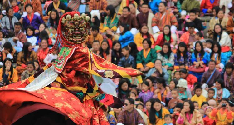 A masked dancer in vibrant costume performs before a large crowd at a traditional festival.