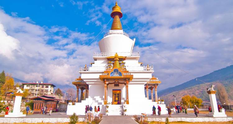 A gleaming white stupa with golden spire rises against a bright sky, visited by scattered tourists.