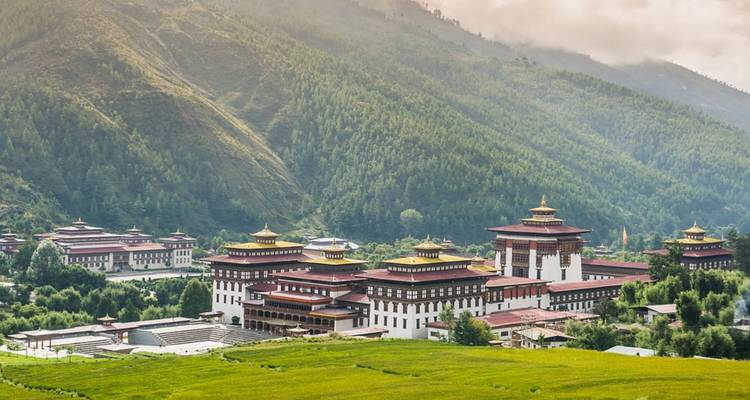A grand Bhutanese dzong with red roofs and golden pinnacles nestles in a green valley.