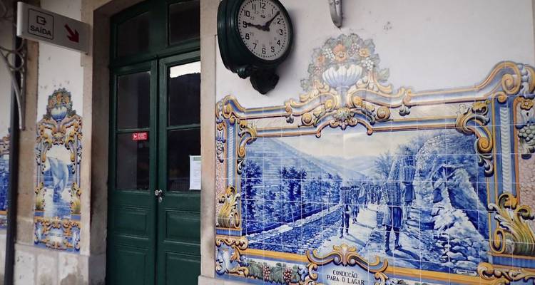 Les murales traditionnelles en carreaux azulejos bleu et blanc ornent l'extérieur d'une petite gare ferroviaire portugaise dotée d'une horloge vintage au-dessus d'une porte verte.