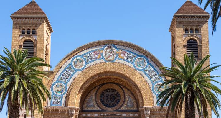 Facade of a brick and mosaic church flanked by palm trees under a clear sky in Oran.