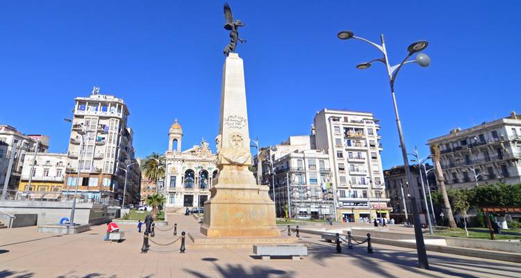Open square in Oran featuring a tall column topped with an eagle statue and surrounding colonial buildings.