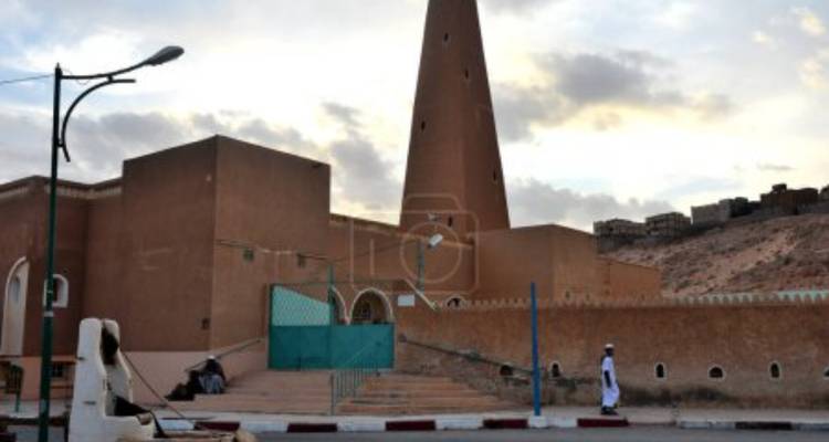 Conical minaret of the Ghardaia Great Mosque rises above adobe buildings at dusk.