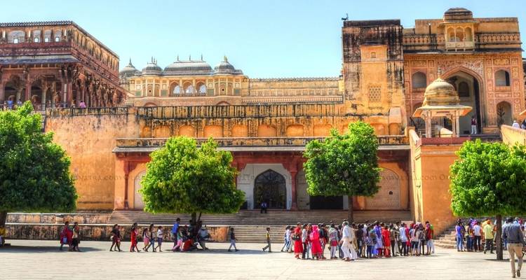 Courtyard of Amber Fort with visitors beneath ochre and pink ramparts.