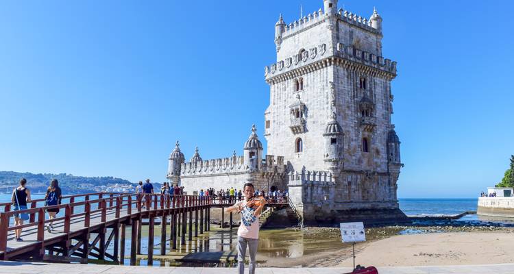 Belémtoren aan de rivieroever met bezoekers die de houten brug oversteken en een violist die optreedt