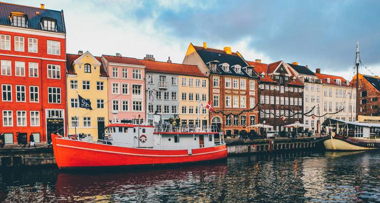 Traditionelle farbenfrohe Stadthäuser und ein rotes Boot, das entlang des Nyhavn-Kanals bei bewölktem Himmel vertäut ist.