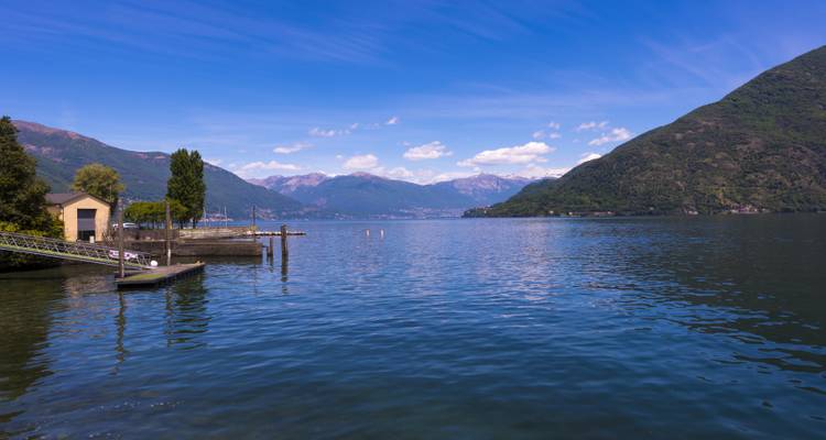 Calm lake surface with small dock and tree-covered hills under a bright blue sky.