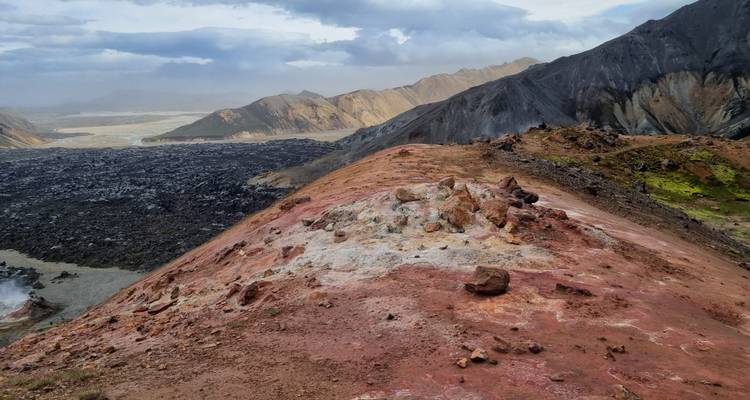 Crête volcanique rougeâtre au terrain déchiqueté se détachant sur des plaines de lave sombres au loin.