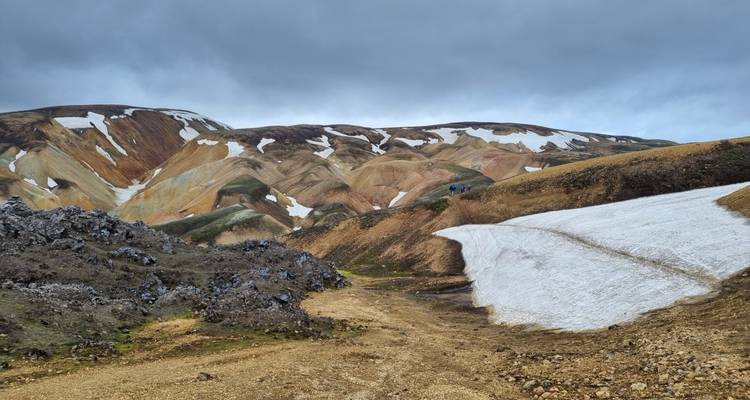 Collines de rhyolite ondulantes partiellement couvertes de plaques de neige sous un ciel morne.