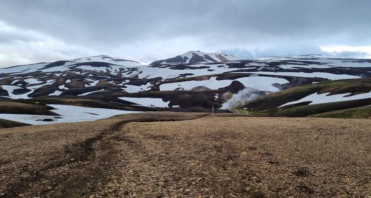Plateau volcanique désolé avec piste de terre sinueuse au milieu des hautes terres parsemées de neige.