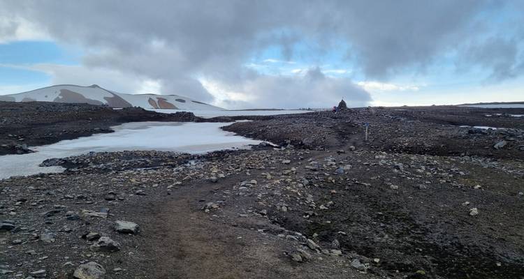 Sentier rocailleux serpentant à travers des plaques de glace et des débris volcaniques sous de bas nuages.