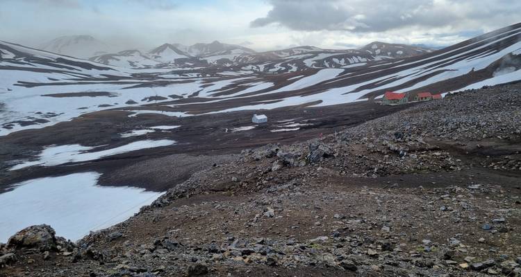 Refuges de montagne isolés et tentes dispersées sur un plateau volcanique tacheté de neige.