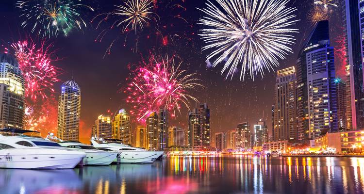Farbenfrohe Feuerwerke über der Skyline von Dubai Marina mit Yachten, die sich nachts im Wasser spiegeln.