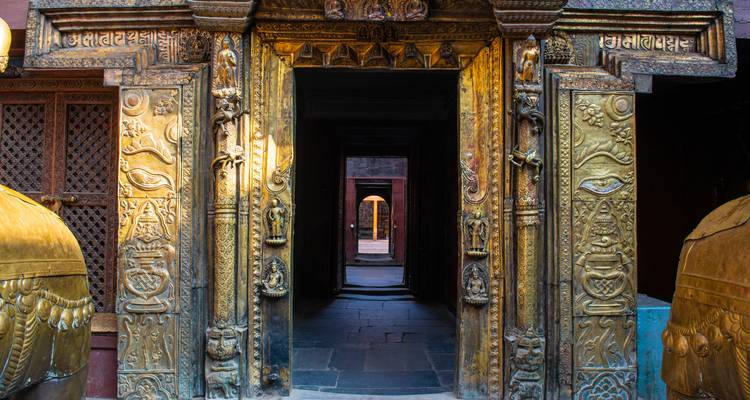 Verzierter goldener Eingang, der zu einer Abfolge von dunklen Gängen in einem Tempel in Kathmandu führt.