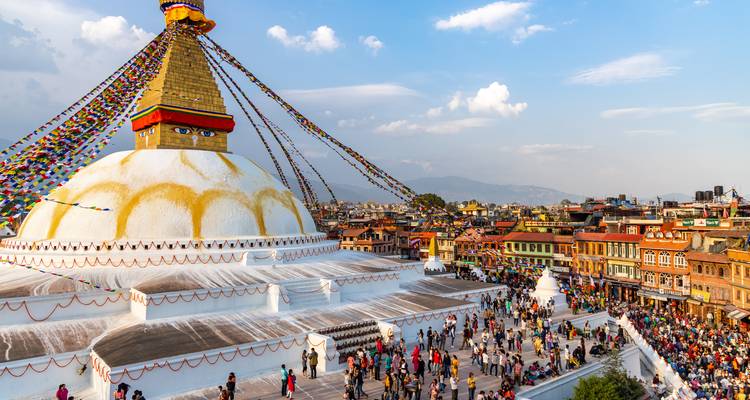 Luftaufnahme der weißen Kuppel und Gebetsfahnen der Boudhanath Stupa, umgeben von lebhaften Straßen.