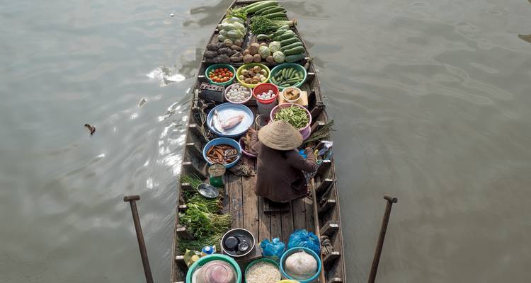 Vendor arranges colourful produce on a wooden boat at a floating market.