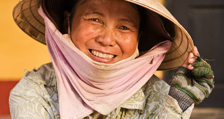 Close-up portrait of a smiling Vietnamese woman wearing a traditional conical hat.