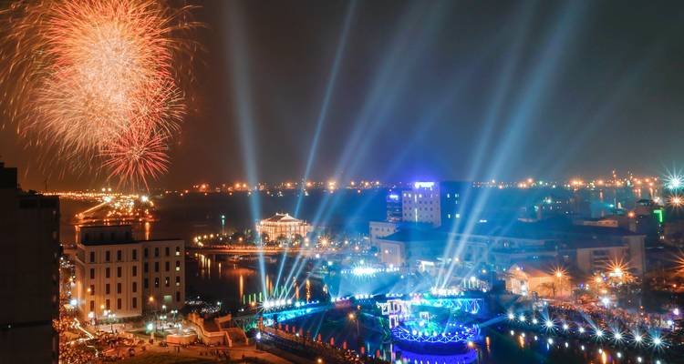 Nighttime festival with fireworks and laser lights reflecting over a waterfront city.