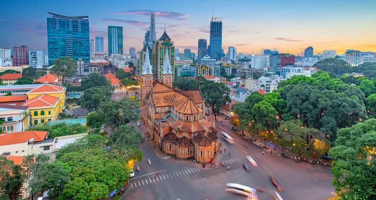 Ho Chi Minh City's Notre-Dame Cathedral stands amid modern skyscrapers at dusk.