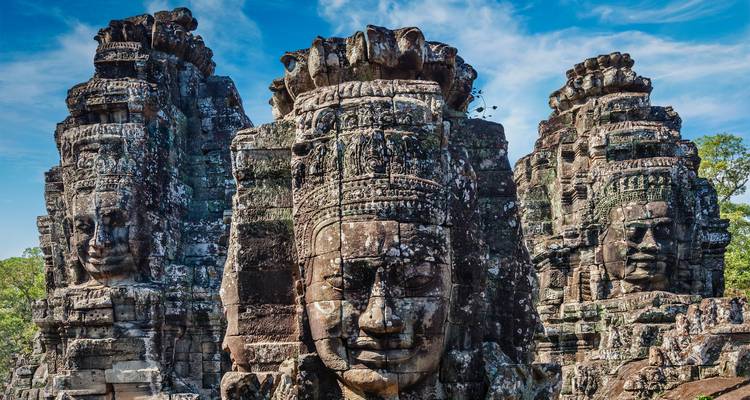 Nahaufnahme von riesigen geschnitzten Steingesichtern des Bayon-Tempels vor blauem Himmel.