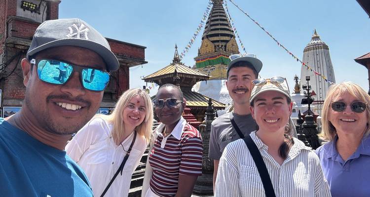 Smiling travellers take a selfie in front of Swayambhunath stupa adorned with prayer flags.