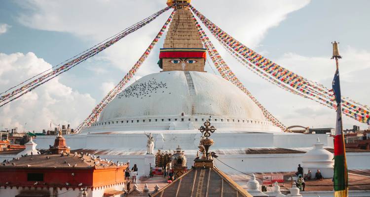 The massive white dome of Boudhanath Stupa draped in colourful prayer flags under a bright sky.