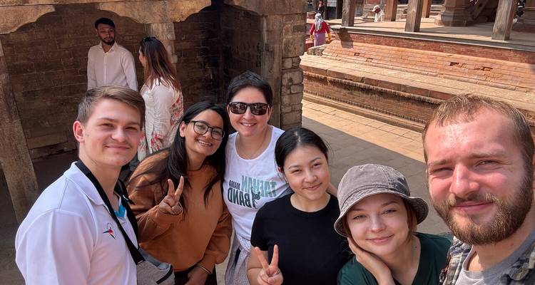Group selfie of young travellers flashing peace signs inside an ancient brick courtyard.