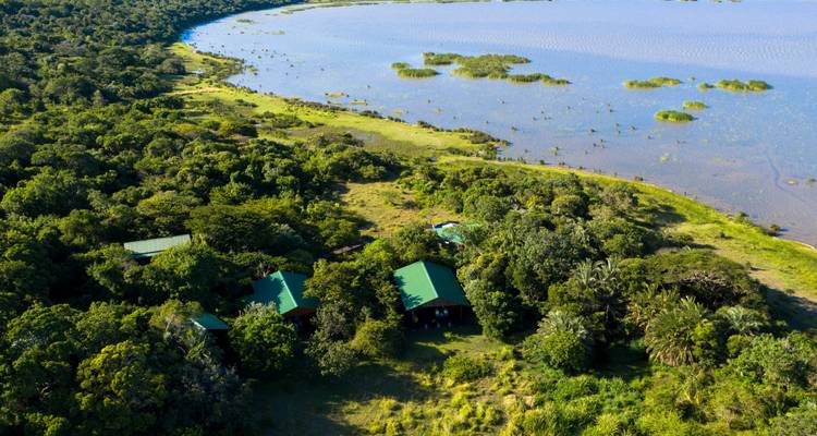 Vue aérienne d'un éco-lodge forestier au bord d'un lac avec des toits verts près d'un lagon.