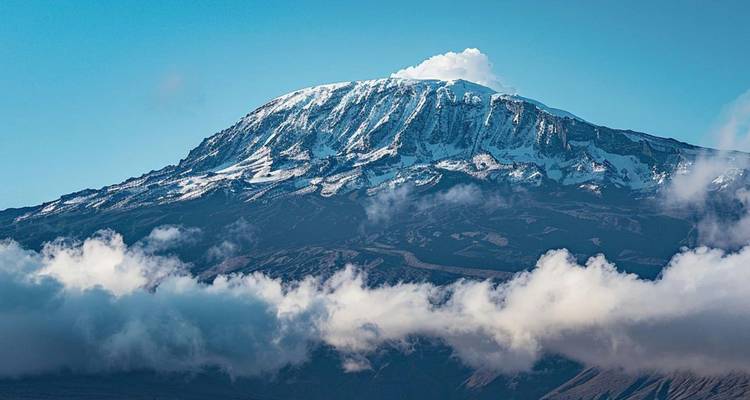 Striking view of snow-capped Mount Kilimanjaro emerging above clouds against a vivid blue sky.