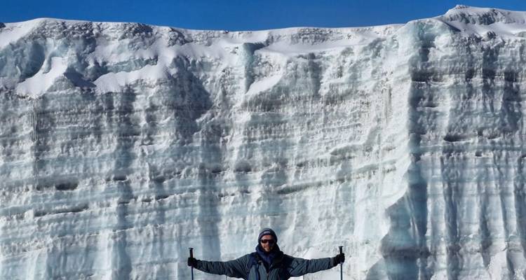 Trekker stands triumphant before a towering blue glacier wall on Kilimanjaro.