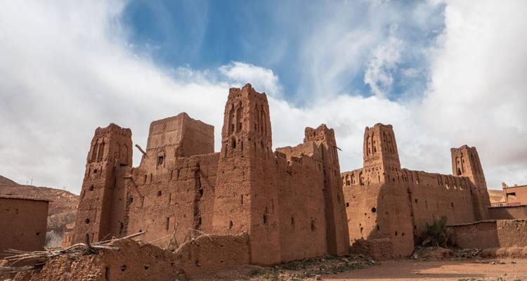 Zerfallende Lehmziegel-Kasbah-Ruinen inmitten dramatischer roter Felsformationen