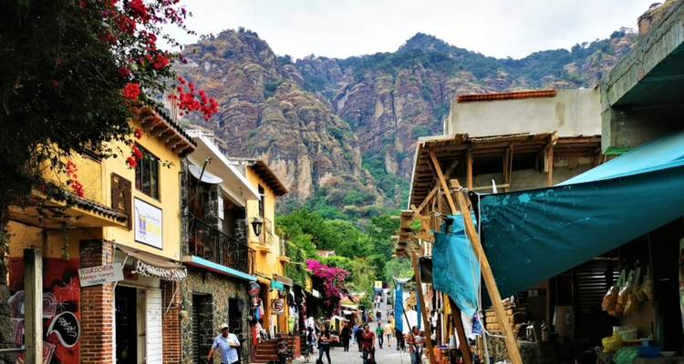 Charming street lined with colorful buildings and stalls leading toward dramatic rocky cliffs