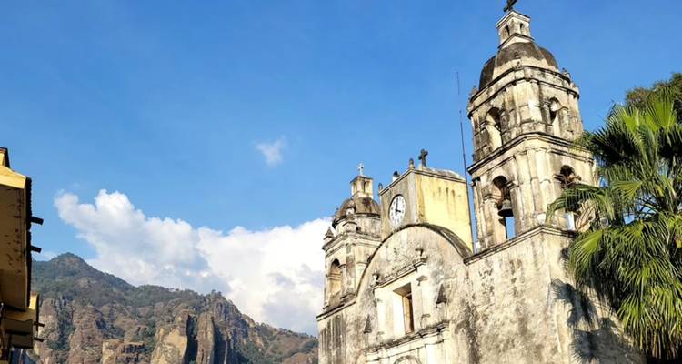 Stone colonial church towers rising against a vivid blue sky with rugged mountains in the background.