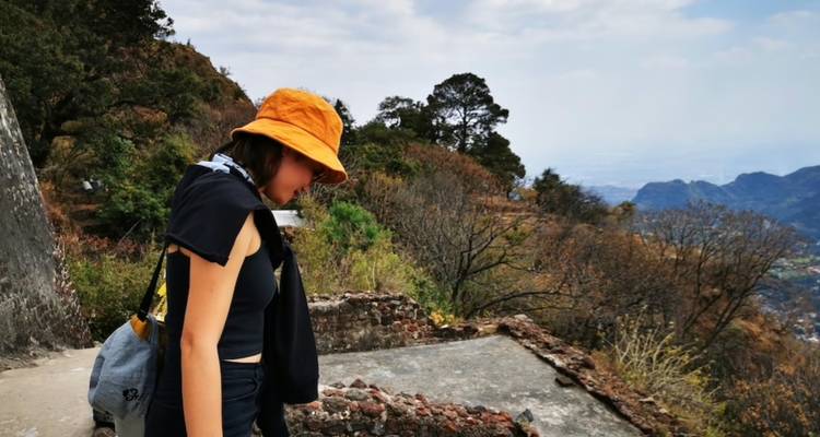Young woman wearing an orange hat walking a rocky mountain trail with expansive valley views.