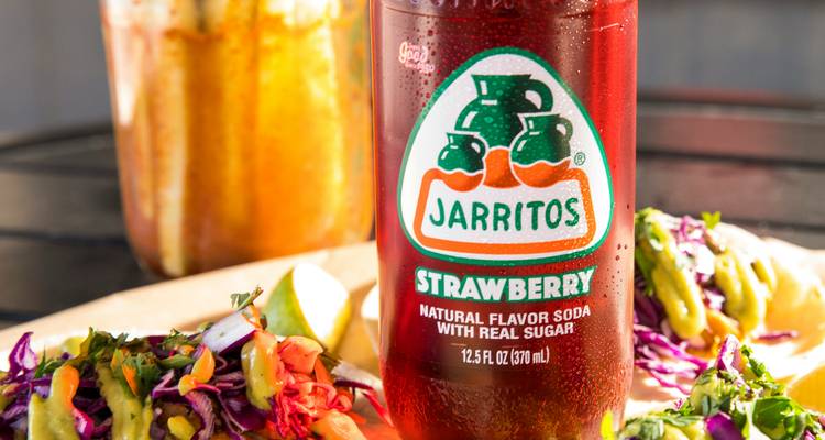 Flasche Jarritos Erdbeerlimonade auf einem Teller mit lebendiger mexikanischer Straßenküche.