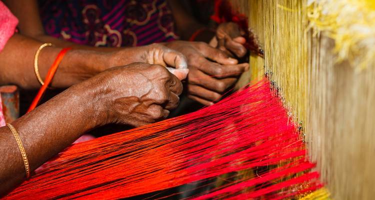 Gros plan de mains expérimentées tissant des fils de soie rouge vif et jaune sur un métier à tisser traditionnel.