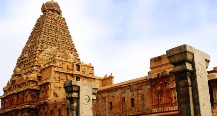The towering vimana of Brihadeeswarar Temple rises above weathered stone walls against a blue sky.