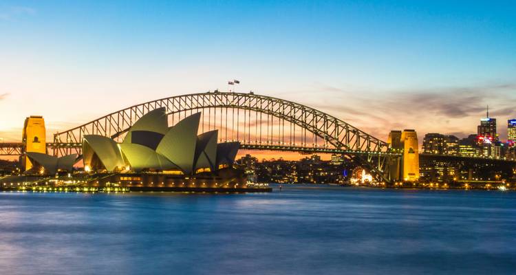 Sydney Opera House and Harbour Bridge illuminated at dusk across smooth harbour waters