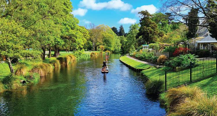 People punting along a tranquil tree-lined river in Christchurch on a bright day with blue skies.