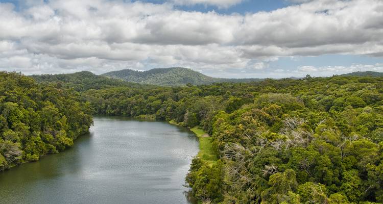 Wide river winding through dense tropical rainforest beneath a partly cloudy sky.