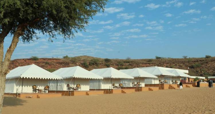Row of luxury desert tents pitched on golden sand beneath a bright morning sky.