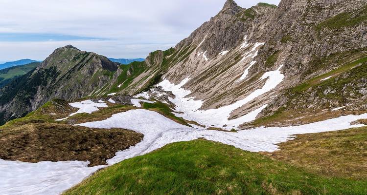Ladera alpina con campos de nieve persistente, crestas rocosas y parches de hierba verde
