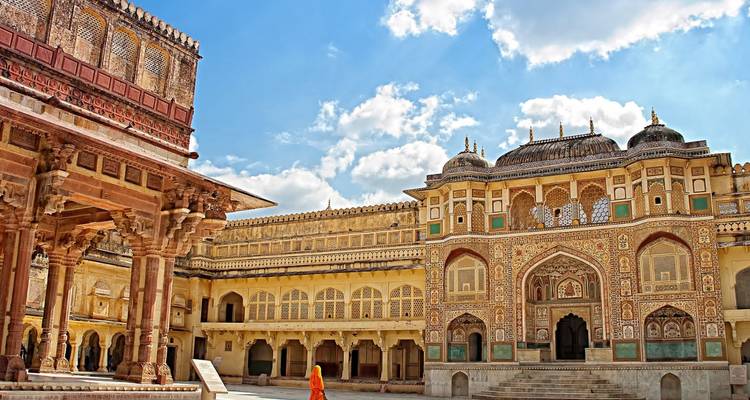 Intricately decorated inner courtyard of Amber Fort with a lone visitor in orange robes