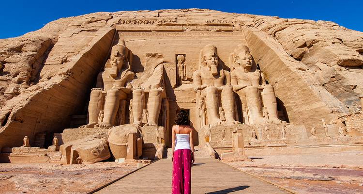 Ein einsamer Reisender geht auf die kolossalen sitzenden Statuen des Abu-Simbel-Tempels unter einem klaren Himmel zu.