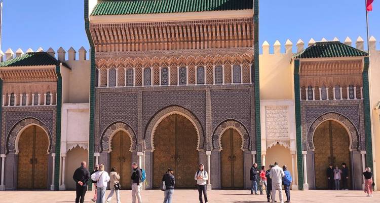 Tourists gathered outside an ornate Moroccan gate with intricate tiles and large golden doors.