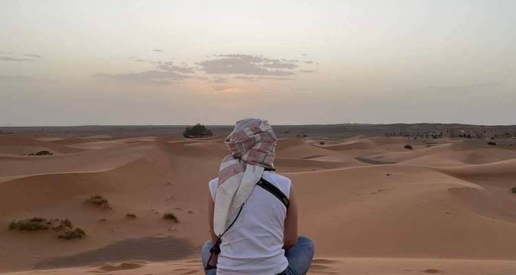Traveller seated quietly facing sunrise over smooth desert dunes.