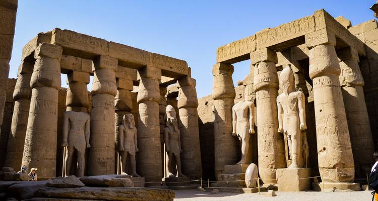 Beeindruckende Sandsteinsäulen und stehende Statuen im Inneren des Luxor-Tempels, beleuchtet von der Nachmittagssonne.