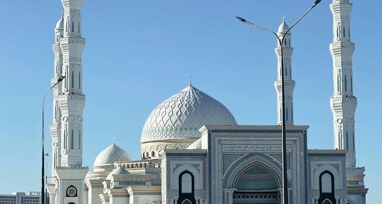 Mosquée élégante aux teintes blanches et bleues dotée de carrelages complexes et de hauts minarets se dressant contre un ciel dégagé.