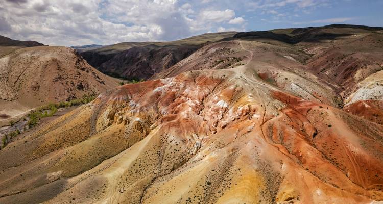 Terres stériles aux rayures colorées de collines roulantes rouges, orange et blanches sous un ciel partiellement nuageux.